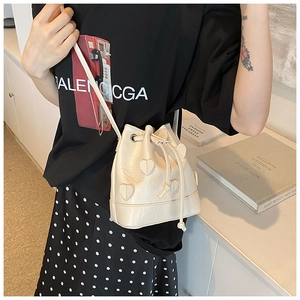 Close-up of ivory drawstring bucket bag featuring sweet heart-shaped leather appliques
