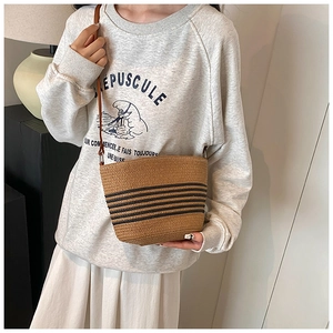 Détail du sac seau en paille marron avec rayures noires et bandoulière en cuir