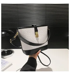 Detail of contrast bucket bag with crocodile texture, gold lock, and dual straps