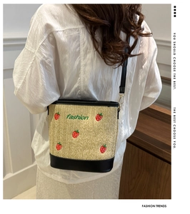 Detail of straw bucket bag featuring strawberry embroidery and crossbody strap worn by model