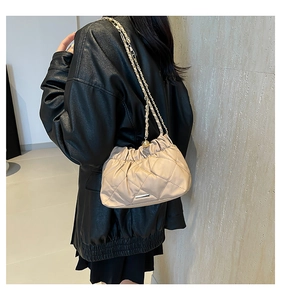 Dettaglio borsa a tracolla beige trapuntata con catena dorata su giacca di pelle nera