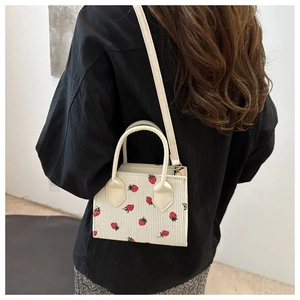 Detail of white corduroy crossbody bag with strawberry print worn by a model