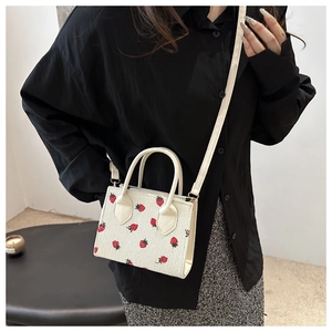 Detail of cream corduroy tote bag with red strawberry print and golden metal hardware
