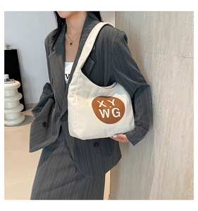 Close-up of beige canvas tote with round leather patch and lettering on model attire