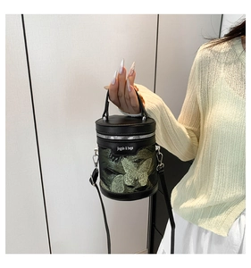 Dettaglio della borsa a secchiello nera cilindrica con ricamo farfalla verde e zip argento