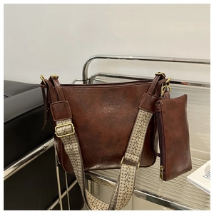 Close-up of vintage brown leather bucket bag with patterned woven strap and gold hardware