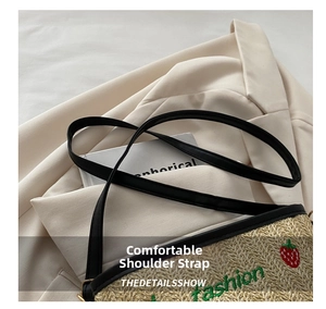 Detail view of woven straw bag with strawberry embroidery and black leather strap