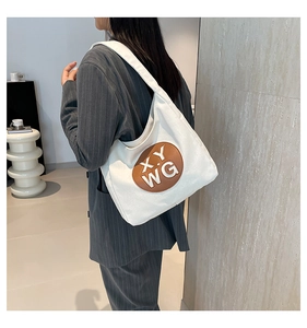 Detail of white canvas tote bag with embossed brown patch on shoulder of a model