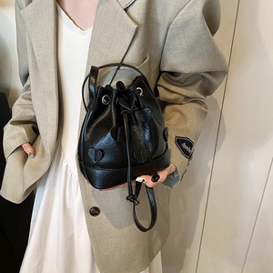 Minimalist black drawstring bucket bag with leather heart patches shown on a model