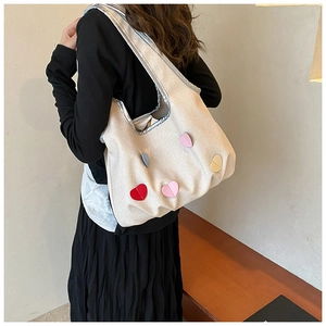 Detailansicht einer großen beigen Canvas-Tasche mit bunten Herz-Patches an der Schulter
