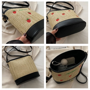 Detail of strawberry embroidery and black PU leather stitching on a straw bucket bag
