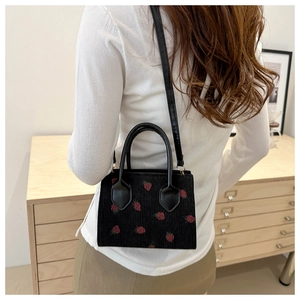 Black corduroy tote bag with red strawberry pattern shown on a female model