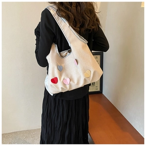 Schulteransicht einer beigen Canvas-Tasche mit bunten Herz-Patches und Silberverzierung