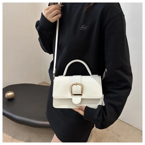 Sac bandoulière chic en cuir blanc avec boucle en fer à cheval dorée porté par le modèle