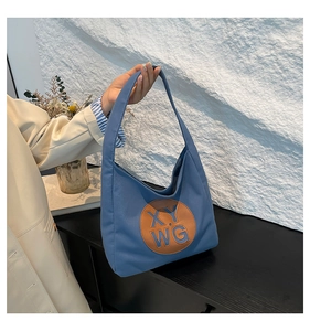 Close-up of blue canvas tote bag with brown leather embossed logo and chic folded design