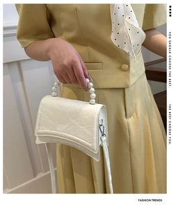 Detail of white textured leather handbag with decorative pearl handle and flap closure