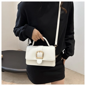 Détail d'un sac à bandoulière carré blanc avec boucle en métal doré et texture lisse