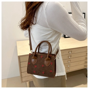 Detailed texture of brown corduroy bag with strawberry embroidery and leather handle