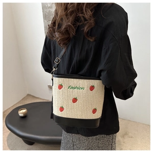 Close-up of strawberry embroidery on woven straw bucket bag with black leather strap