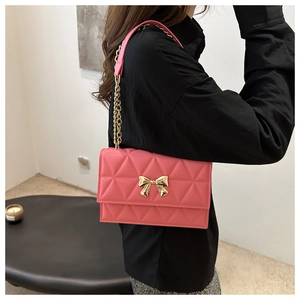 Detailed shot of pink quilted crossbody bag featuring a golden bow buckle and chain strap