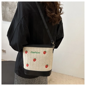 Detail of strawberry embroidery and fashion text on straw bucket bag with black strap