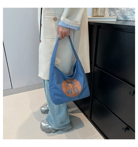 Blue canvas tote bag with brown leather XY WG patch shown on a shoulder-worn model