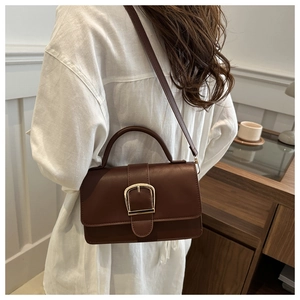 Sac à bandoulière vintage en cuir marron avec boucle dorée porté par un mannequin chic