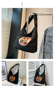 Detail of a black canvas tote bag featuring a round brown patch with XY WG lettering