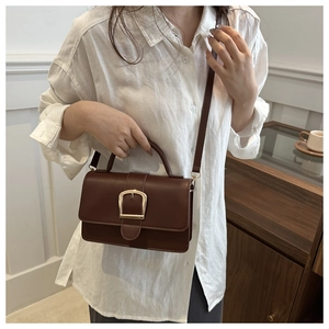 Détail d'un sac bandoulière vintage marron avec boucle en fer à cheval dorée et poignée