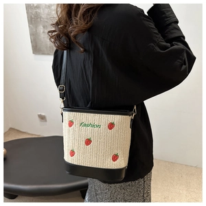 Detail of straw bucket bag with strawberry embroidery and black leather trim