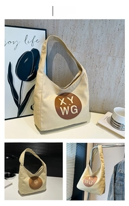 Detail of canvas tote bag featuring brown leather patch with embossed XY WG lettering