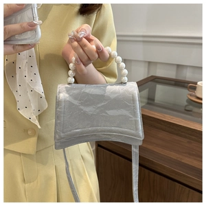 Detail of silver pearl handle handbag with a crescent base and shiny pleated texture