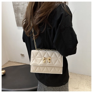 Detail of a beige quilted crossbody bag with a gold bow buckle worn by a model