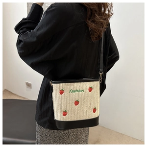 Detail of strawberry embroidery on woven bucket bag with black leather trim and strap