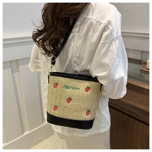 Detailed view of strawberry embroidery and woven texture on a straw bucket bag