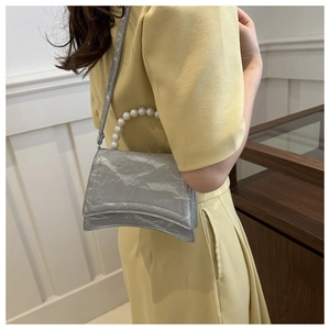 Detail of silver metallic pleated handbag featuring a curved base and pearl handle