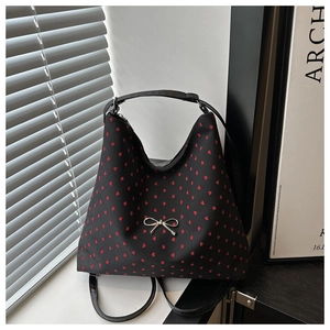 Détail d'un sac cabas noir avec motifs de cœurs rouges et boucle en nœud argenté