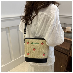 Close-up of strawberry embroidery on beige straw bucket bag with adjustable black strap
