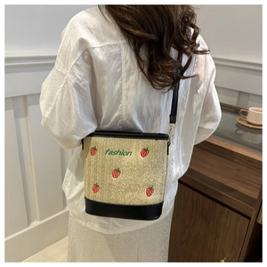 Detail of straw bucket bag featuring red strawberry embroidery and green fashion text