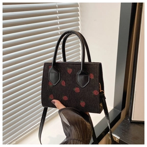Close-up of black corduroy handbag with red strawberry embroidery and detail strap