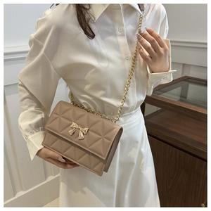 Quilted beige shoulder bag with golden bow buckle shown on model in home setting