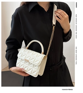 Detail of white quilted crossbody bag with golden chain and woven handle on black outfit