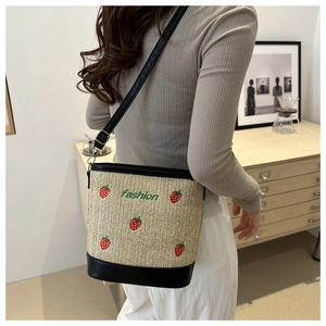 Detail of straw bucket bag featuring strawberry embroidery and black leather strap