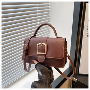 Gros plan détaillé du sac bandoulière en cuir marron foncé avec boucle dorée en fer