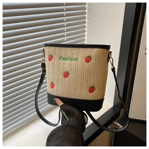Detail of hand-woven straw bucket bag with strawberry embroidery and leather strap