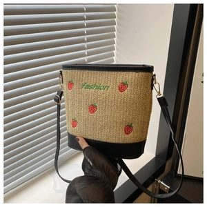 Detail of strawberry embroidery and black leather trim on a woven straw bucket bag