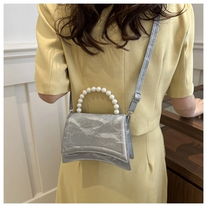 Model showing silver pleated crossbody bag with large pearl handle in home setting