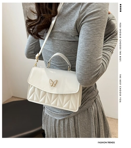 Detail view of a white patent leather shoulder bag featuring a gold butterfly buckle