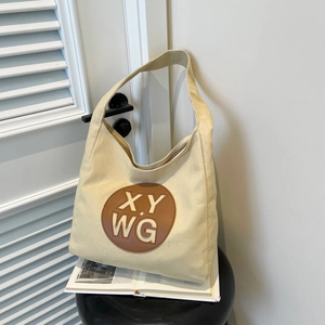 Large beige canvas tote bag with brown leather XY WG patch on a black side table