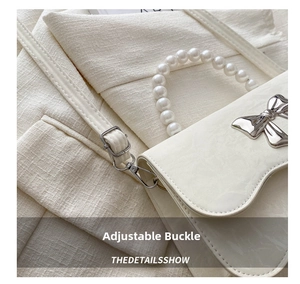 Detail view of adjustable leather strap with silver pin buckle on cream white bag